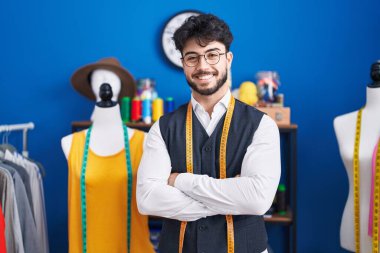 Genç İspanyol terzi gülümsüyor. Kollarını kavuşturup dikiş atölyesinde duruyor.