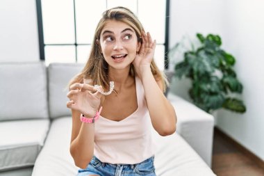 Genç, sarışın bir kadın, görünmez bir hizaya girmiş, ortodontik gülümsüyor. Dedikodulara ve dedikodulara kulak veriyor. Sağırlık kavramı. 