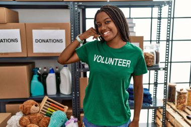 Bağışlarda gönüllü tişört giyen genç Afrikalı Amerikalı kadın gülümsüyor telefonla el ve parmaklarıyla telefonla konuşuyor gibi yapıyor. iletişim kavramları. 