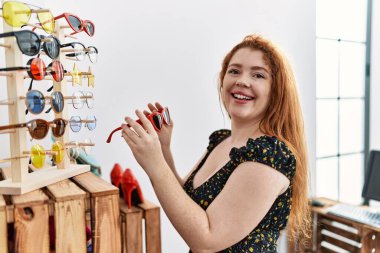 Genç kızıl saçlı kadın güneş gözlüğü dükkanından alışveriş yapıyor.