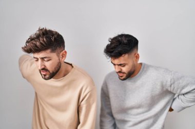 Young homosexual couple standing over white background suffering of backache, touching back with hand, muscular pain 