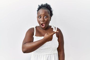 İzole edilmiş beyaz arka planda duran genç Afrikalı kadın parmağını yana çevirerek şaşırdı, ağzı açık hayret içinde kaldı.. 