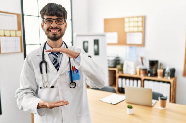 Doktor üniforması giyen sakallı İspanyol bir adam ve ellerinde büyük ve büyük bir işaret işareti olan steteskop ile ofiste. Ölçüm sembolü. Kameraya bakıp gülümsüyor. ölçüm kavramı. 