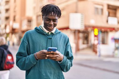 Sokakta akıllı telefon kullanan, kendinden emin gülümseyen Afrikalı Amerikalı bir adam.