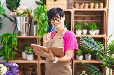 Middle age chinese woman florist smiling confident reading notebook at flower shop