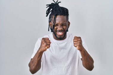 Beyaz arka plan üzerine günlük tişört giyen Afrikalı bir adam başarılı olduğu için heyecanlı kolları havada ve gözleri kapalı zaferi kutlarken gülümsüyor. Kazanan konsept. 