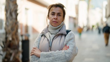 Orta yaşlı İspanyol kadın ciddi bir ifade ve kollarını kavuşturarak caddede duruyor.