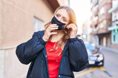 Young blonde woman wearing medical mask standing at street