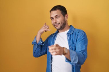 Sarı arka planda durup gülümseyen İspanyol bir adam telefonla konuşuyor ve seni işaret ediyor. Ara beni.. 