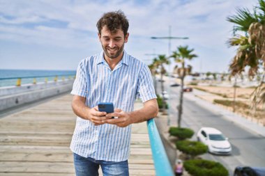 Genç İspanyol adam güvertede akıllı telefon kullanarak mutlu bir şekilde gülümsüyor..