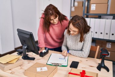 Two women ecommerce business workers writing on document at office