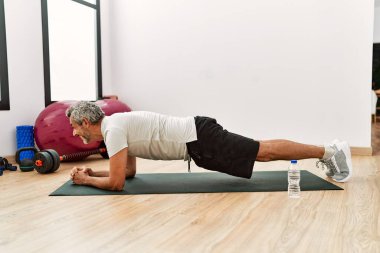 Orta yaşlı, gri saçlı, gülümseyen, spor merkezinde kendine güvenen karın kasları egzersizi yapan adam.