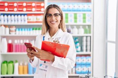 Genç sarışın eczacı eczanede akıllı telefon okuma belgesi kullanıyor.