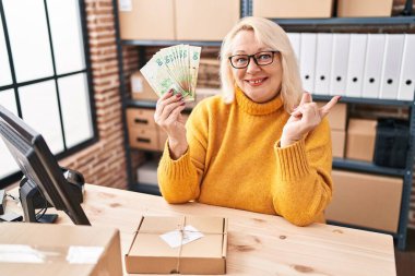 Orta yaşlı beyaz bir kadın küçük işletmelerde çalışıyor elinde Hong Kong dolarları tutarak mutlu bir şekilde elini ve parmağını kenarda gezdiriyor. 