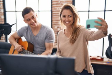 Klasik gitar dersi alan erkek ve kadın müzisyenler müzik stüdyosundaki akıllı telefondan selfie çekiyorlar.