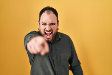 Plus size hispanic man with beard standing over yellow background pointing displeased and frustrated to the camera, angry and furious with you 
