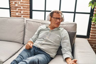 Middle age man listening to music sitting on sofa at home