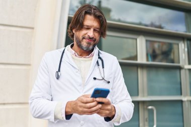 Hastanedeki akıllı telefonu kullanarak gülümseyen orta yaşlı bir doktor.