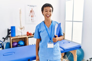 Kısa saçlı, İspanyol bir kadın ağrı kesici kliniğinde çalışıyor. Seksi bir ifadeyle kameraya bakıyor. Neşeli ve mutlu bir yüzü var.. 