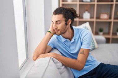 Evinde ciddi bir ifadeyle koltukta oturan Latin asıllı genç adam.