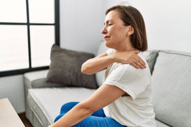 Orta yaşlı İspanyol bir kadın evinde boynu ağrıyan bir kanepede oturuyor.