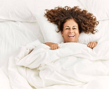 Orta yaşlı İspanyol kadın mutlu bir şekilde gülümsüyor yatak odasında yatarken.