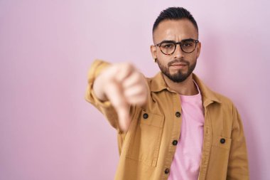Pembe arka planda duran Latin kökenli genç adam mutsuz ve kızgın görünüyor. Reddedilmiş ve olumsuz bir hareket sergiliyor. kötü ifade. 