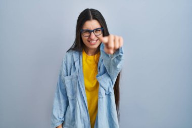 Young hispanic woman standing over blue background pointing displeased and frustrated to the camera, angry and furious with you 
