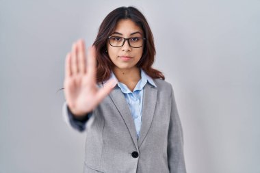 Hispanic young business woman wearing glasses doing stop sing with palm of the hand. warning expression with negative and serious gesture on the face. 
