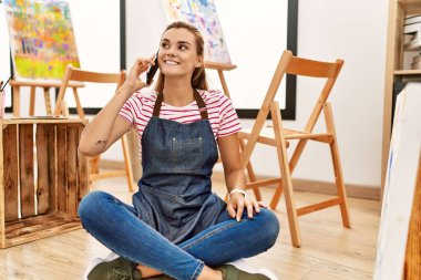 Sanat stüdyosundaki akıllı telefondan konuşan kendine güvenen genç bir kadın.