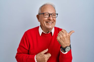 İzole edilmiş arka planda gri saçlı yaşlı bir adam gülümsüyor ve başparmağıyla yan tarafa bakıyor.. 