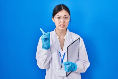 Laboratuvarda çalışan Çinli genç bir kadın endişeli ve endişeli bir ifadeye işaret ediyor. 