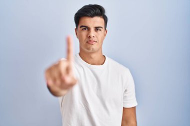 Mavi arka planda dikilen İspanyol adam parmağını kaldırmış ve kızgın bir ifadeyle işaret ediyor, hiçbir hareket göstermiyor. 