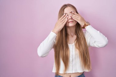 Pembe arka planda duran beyaz bir kadın yorgunluk ve baş ağrısı için gözlerini ovuşturuyor, uykulu ve yorgun bir ifade. görme sorunu 