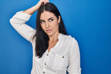 Mavi arka planda dikilen genç İspanyol kadın kafasını karıştırıyor ve soruyu merak ediyor. Şüpheyle kararsız, kafa kafaya düşünerek. Düşünceli kavram. 