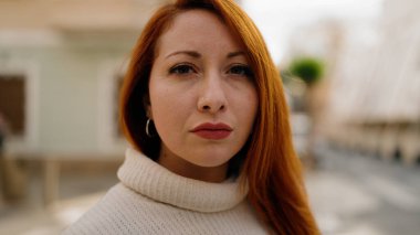 Sokakta ciddi bir ifadeyle duran genç kızıl saçlı kadın.