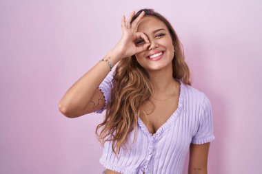 Pembe arka planda duran genç İspanyol kadın el hareketleriyle gülümsüyor ve mutlu yüzüyle parmaklarının arasından bakıyor.. 