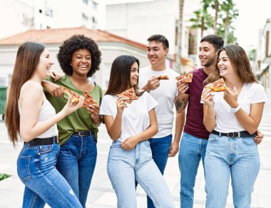 Group of young friends smiling happy eating pizza standing at the city.