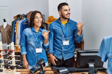 Perakende mağazasında çalışan, mutlu yüzüyle gülümseyen ve baş parmağıyla yan tarafı gösteren genç ırklar arası insanlar.. 