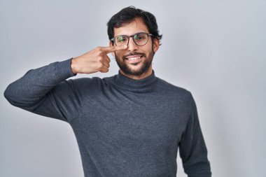 Handsome latin man standing over isolated background pointing with hand finger to face and nose, smiling cheerful. beauty concept 
