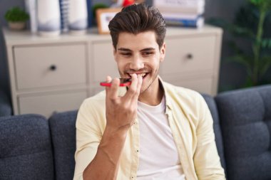 Young hispanic man talking on the smartphone sitting on sofa at home