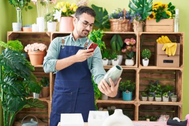 Young hispanic man florist make photo to plant pot by smartphone at flower shop
