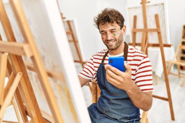 Genç İspanyol adam resim stüdyosunda akıllı telefon çizimi yapıyor.