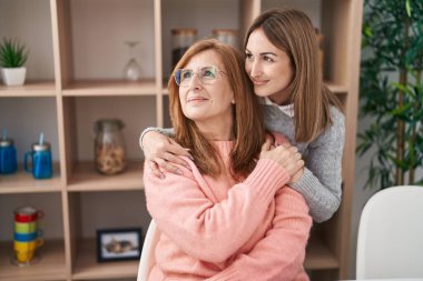 Mother and daughter hugging each other sitting on desk at home