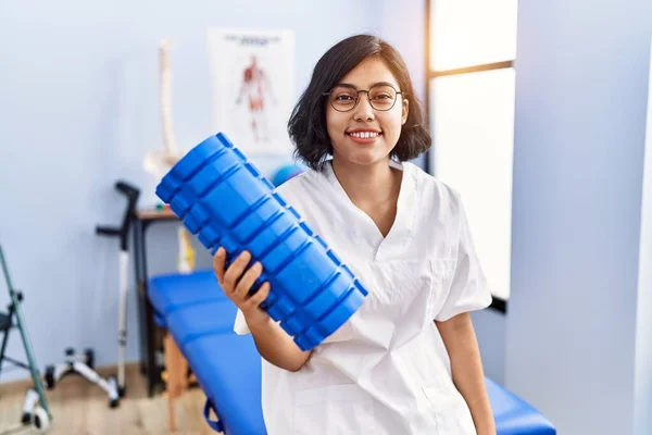 Young Hispanic Physiotherapist Woman Holding Foam Roller Clinic Looking Positive — Stock Photo, Image