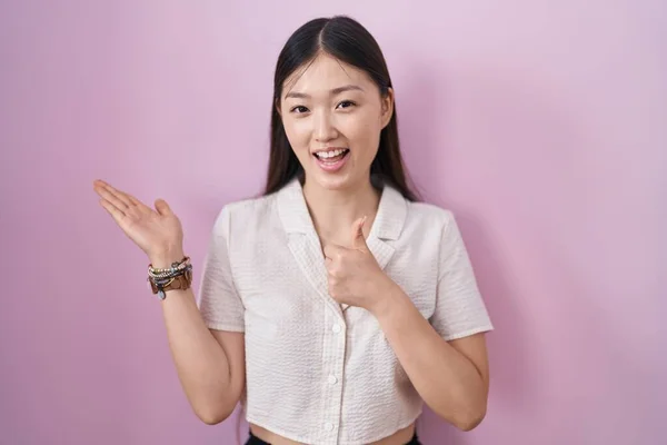 中国年轻女子站在粉红的背景上 手牵着手 竖起大拇指做手势 开心地微笑着 — 图库照片