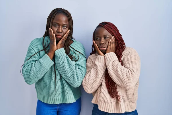 Две Африканки Стоят Синем Фоне Уставшие Руки Покрывающие Лицо Депрессию — стоковое фото
