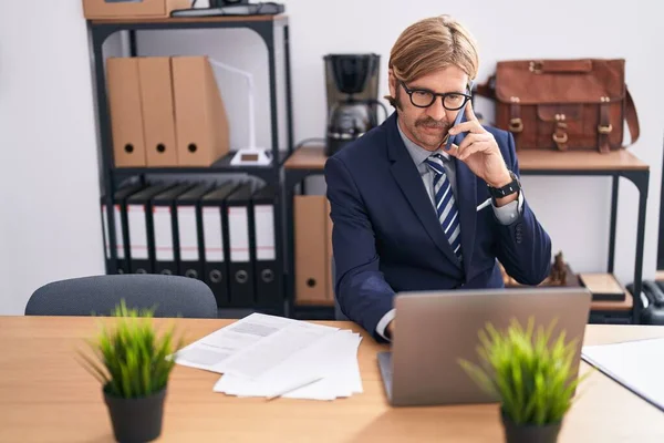 若いブロンド男ビジネス労働者を使用してノートパソコンで話す上でスマートフォンでオフィス — ストック写真