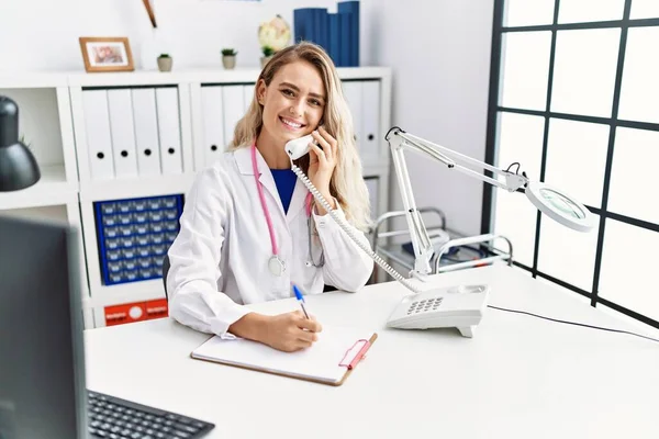 Young Woman Wearing Doctor Uniform Writing Document Talking Telephone Clinic — Stock Photo, Image