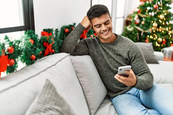 Young Hispanic Man Using Smartphone Sitting Sofa Christmas Tree Home — 스톡 사진